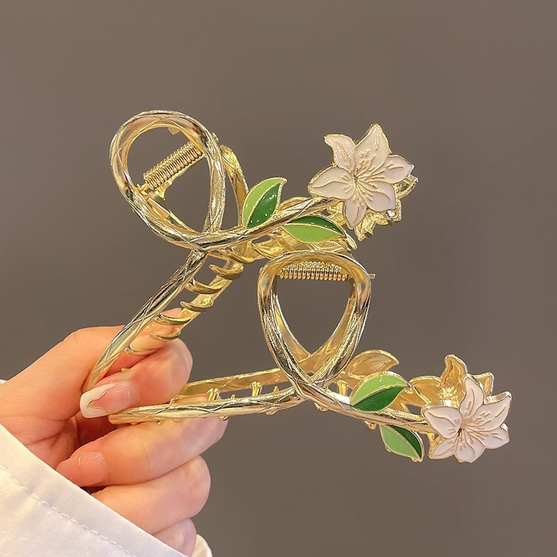 Decorative hair clip with floral design held by a hand against a gray background